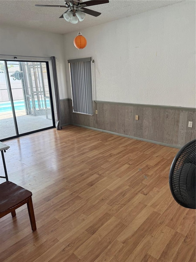2026 Aaron Pl, Clearwater, FL 33760 - spare room featuring a ceiling fan, a textured ceiling, light wood-style flooring, a wainscoted wall, and wood walls