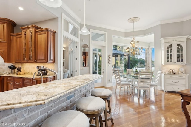 919 Ballinger Rd, Lutz, FL 33548 - kitchen with brown cabinetry, light stone countertops, a breakfast bar area, glass insert cabinets, and a chandelier