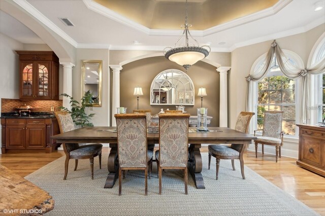 919 Ballinger Rd, Lutz, FL 33548 - dining space featuring a tray ceiling, light wood finished floors, decorative columns, arched walkways, and crown molding