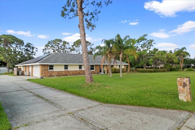 903 Tomahawk Trl, Brandon, FL 33511 - single story home featuring an attached garage, concrete driveway, a front lawn, roof mounted solar panels, and stone siding
