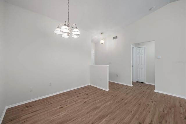 spare room featuring lofted ceiling, a chandelier, wood finished floors, and baseboards