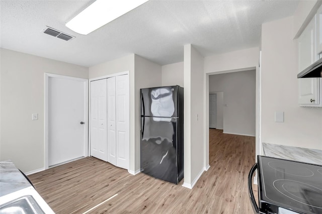 kitchen with black appliances, light wood finished floors, light countertops, white cabinets, and a textured ceiling