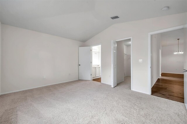 unfurnished bedroom featuring a spacious closet, light colored carpet, lofted ceiling, a chandelier, and a closet