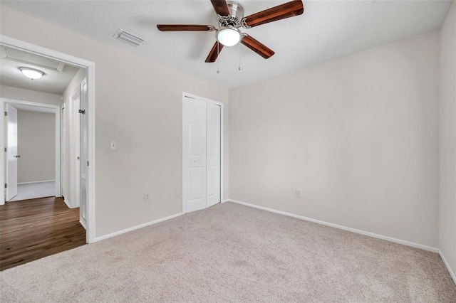 unfurnished bedroom with carpet, baseboards, a closet, attic access, and a ceiling fan