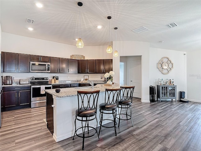 3891 Reflection Dock Dr, Seffner, FL 33584 - kitchen with stainless steel appliances, a kitchen breakfast bar, light wood-type flooring, dark brown cabinets, and pendant lighting