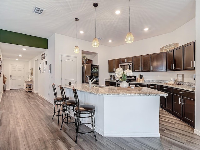 3891 Reflection Dock Dr, Seffner, FL 33584 - kitchen featuring stainless steel appliances, dark brown cabinets, a sink, an island with sink, and light wood-style flooring