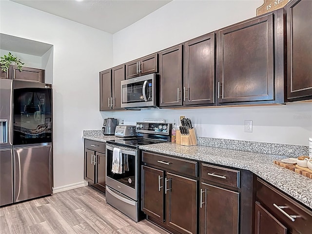 3891 Reflection Dock Dr, Seffner, FL 33584 - kitchen featuring appliances with stainless steel finishes, dark brown cabinetry, light wood-style flooring, and light stone countertops