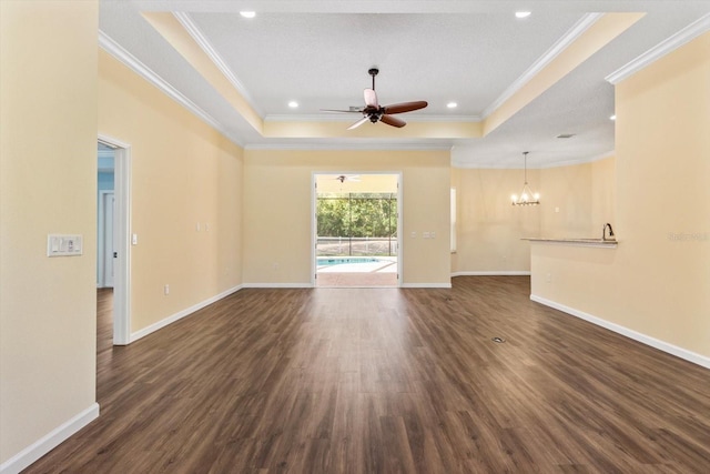 unfurnished living room featuring a tray ceiling, dark wood finished floors, crown molding, a ceiling fan, and a chandelier