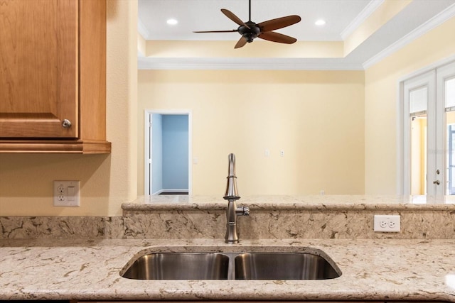 kitchen featuring a sink, crown molding, light stone counters, a ceiling fan, and brown cabinetry