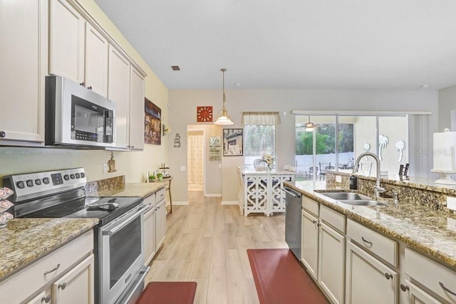 kitchen featuring stainless steel appliances, a sink, light wood-type flooring, hanging light fixtures, and light stone countertops
