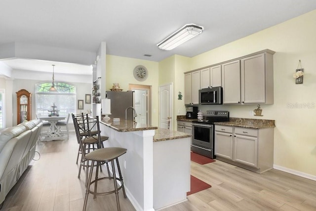 kitchen with stainless steel appliances, a breakfast bar area, light wood finished floors, dark stone counters, and gray cabinetry