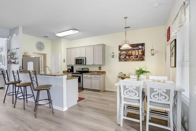 kitchen featuring appliances with stainless steel finishes, light wood-style flooring, a kitchen breakfast bar, dark stone counters, and decorative light fixtures