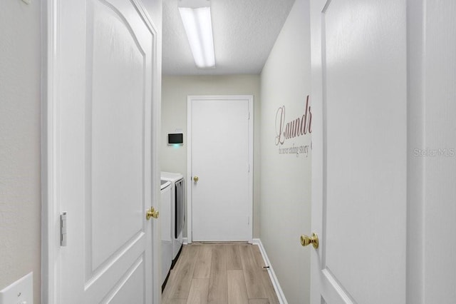 hall with washing machine and clothes dryer, light wood-style flooring, baseboards, and a textured ceiling