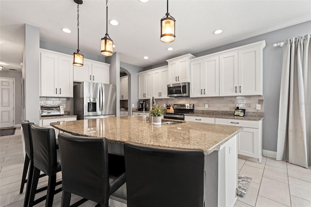 1436 30th Ave N, Saint Petersburg, FL 33704 - kitchen featuring appliances with stainless steel finishes, arched walkways, decorative backsplash, a center island with sink, and hanging light fixtures