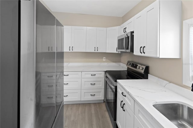 1101 Dr Martin L King Jr Way, Haines City, FL 33844 - kitchen featuring appliances with stainless steel finishes, white cabinets, light stone counters, light wood finished floors, and a sink