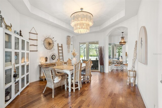dining space featuring a tray ceiling, arched walkways, a chandelier, hardwood / wood-style floors, and french doors
