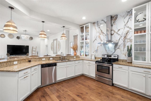 kitchen featuring stainless steel appliances, wall chimney exhaust hood, a sink, white cabinetry, and glass insert cabinets