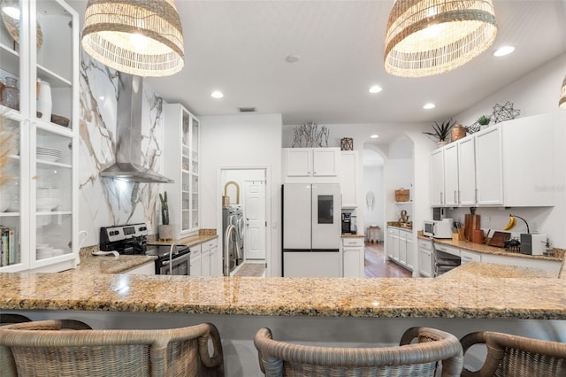 kitchen with white appliances, wall chimney range hood, light stone counters, glass insert cabinets, and recessed lighting