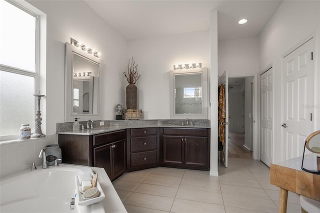 bathroom featuring healthy amount of natural light, tile patterned flooring, a bath, and double vanity