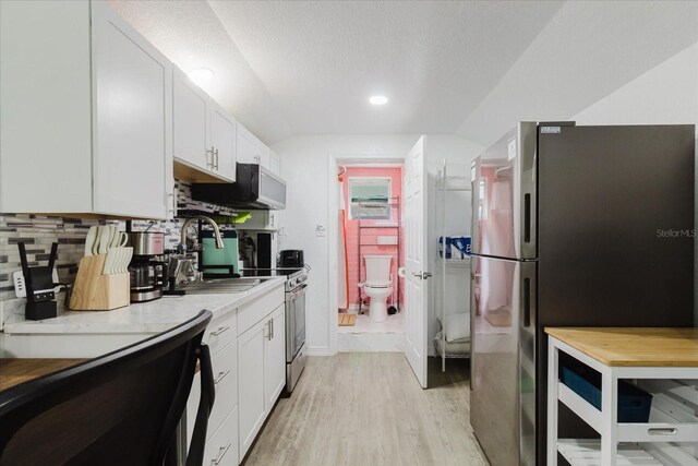 1010 Oakhill St, Seffner, FL 33584 - kitchen with appliances with stainless steel finishes, light wood finished floors, white cabinets, vaulted ceiling, and backsplash