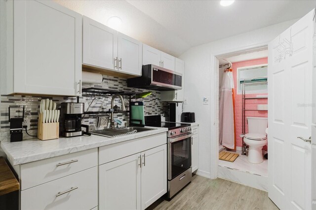 1010 Oakhill St, Seffner, FL 33584 - kitchen with stainless steel appliances, a sink, light wood-style flooring, white cabinets, and decorative backsplash