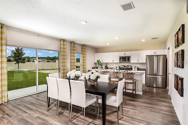 dining space featuring wood finished floors, a textured ceiling, recessed lighting, and baseboards