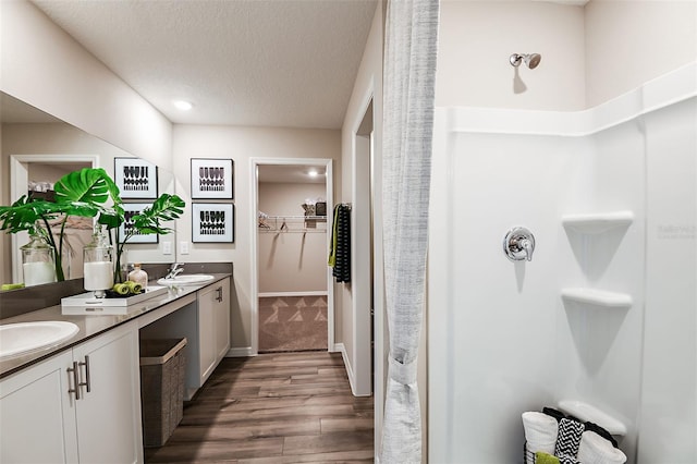 full bath featuring wood finished floors, a shower, a walk in closet, double vanity, and a textured ceiling