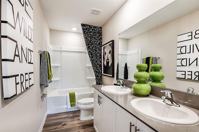 bathroom featuring wood finished floors, toilet, double vanity, and washtub / shower combination