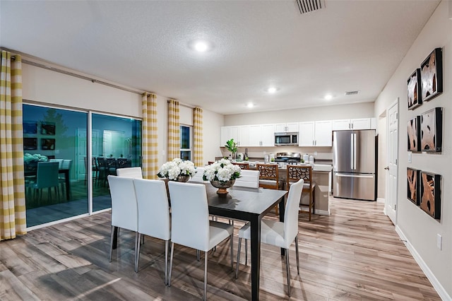 dining area with light wood-style flooring, recessed lighting, a textured ceiling, and baseboards