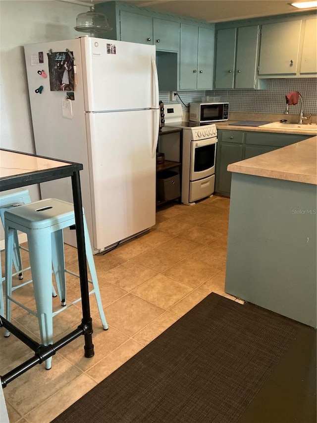 kitchen with white appliances, green cabinetry, light tile patterned floors, a sink, and light countertops