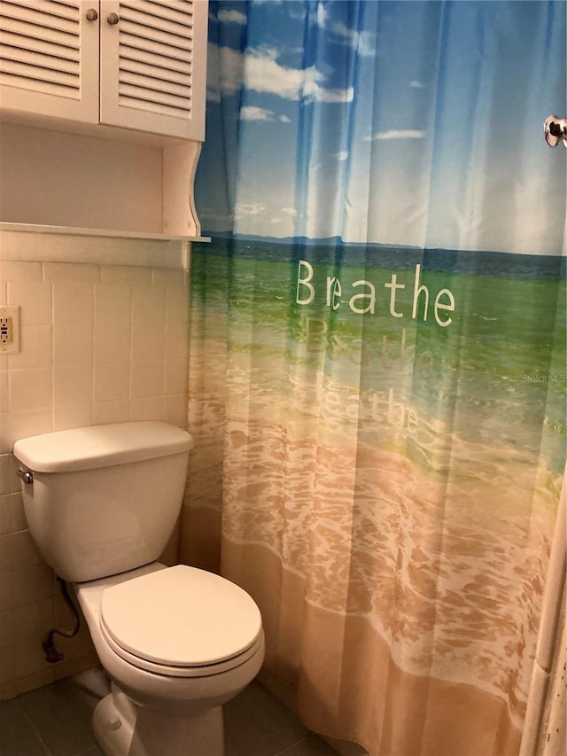 bathroom with tile patterned flooring, toilet, and tile walls