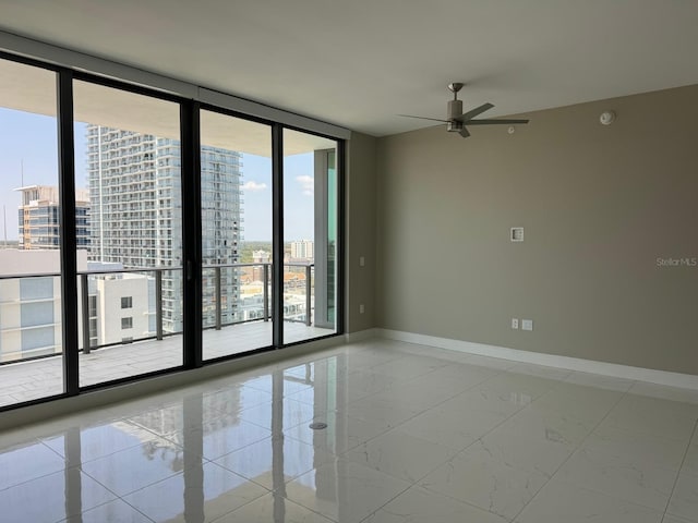empty room featuring healthy amount of natural light, a ceiling fan, baseboards, a city view, and floor to ceiling windows