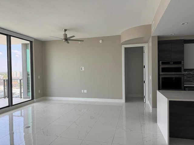 unfurnished living room featuring baseboards, a ceiling fan, light marble finish floors, and expansive windows