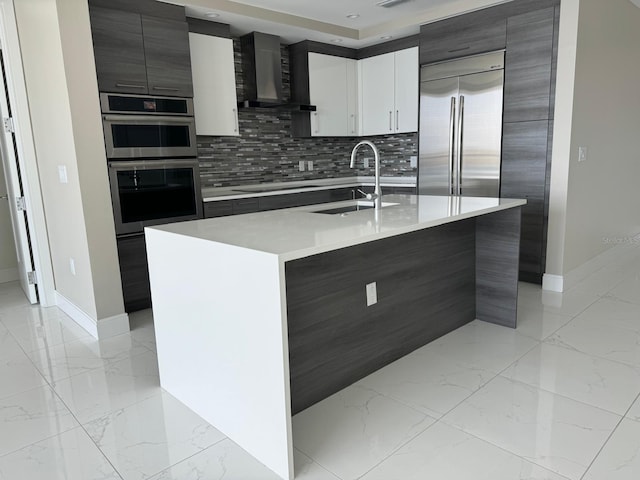 kitchen with wall chimney range hood, a sink, stainless steel appliances, and light marble finish flooring