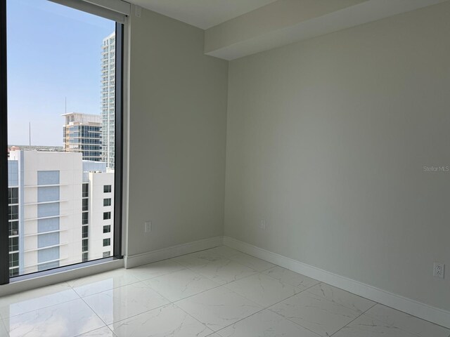empty room with marble look tiles, baseboards, and a city view