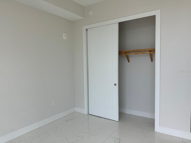 unfurnished bedroom featuring light marble finish flooring, baseboards, and a closet