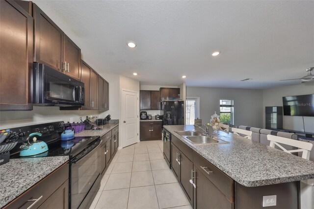 10210 White Linen Ave, Riverview, FL 33578 - kitchen with black appliances, a sink, light tile patterned floors, an island with sink, and dark brown cabinetry