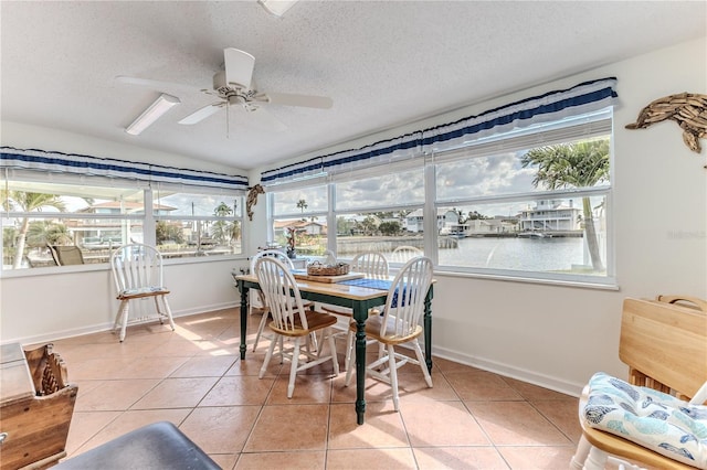sunroom / solarium with tile patterned floors, a textured ceiling, vaulted ceiling, baseboards, and a water view
