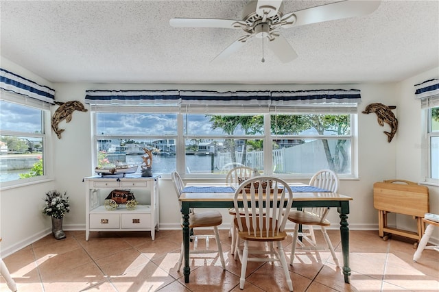 sunroom / solarium with tile patterned flooring, a textured ceiling, a water view, and baseboards