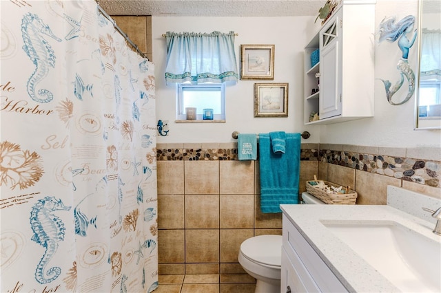 full bathroom featuring tile walls, healthy amount of natural light, toilet, a wainscoted wall, and vanity