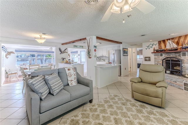 living area featuring light tile patterned floors, a stone fireplace, a ceiling fan, and a textured ceiling