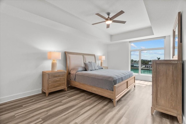 415 Island Way Unit 303, Clearwater Beach, FL 33767 - bedroom with light wood-style flooring, a tray ceiling, baseboards, and ceiling fan