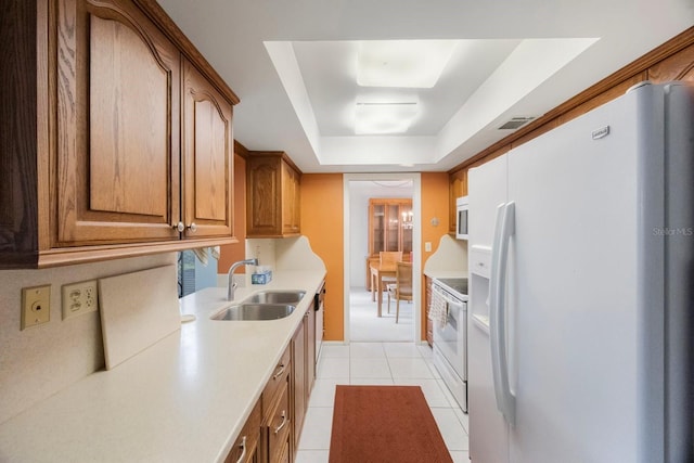 kitchen with white appliances, a sink, light tile patterned floors, light countertops, and a tray ceiling