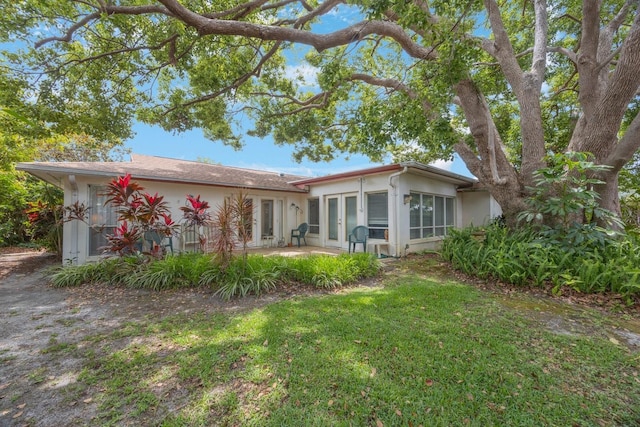 rear view of house featuring french doors, a patio, stucco siding, and a lawn
