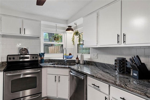 kitchen with appliances with stainless steel finishes, a sink, white cabinetry, and dark stone counters