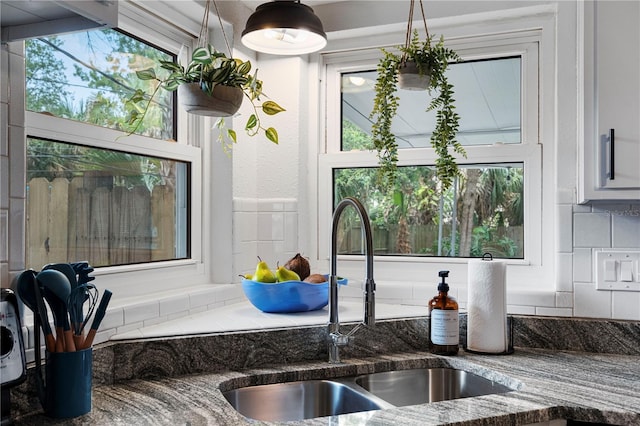 kitchen view of a sink, dark stone countertops, and white cabinets