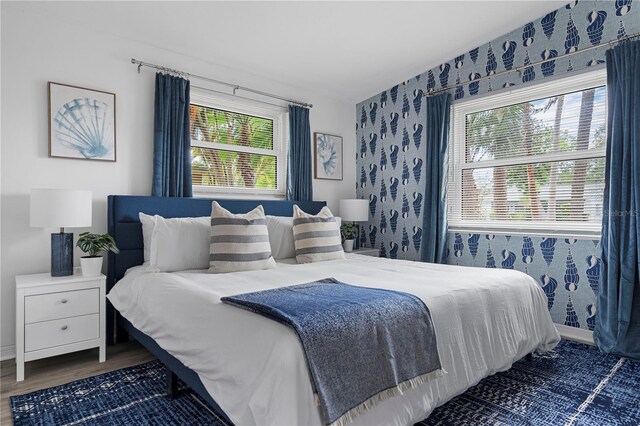 bedroom with wallpapered walls, wood finished floors, multiple windows, and baseboards