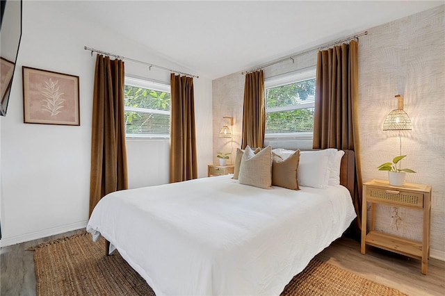 bedroom featuring lofted ceiling, wood finished floors, multiple windows, and baseboards