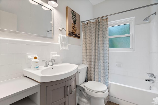 bathroom featuring toilet, shower / bathtub combination with curtain, vanity, tile walls, and a wainscoted wall