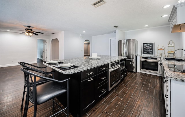 1402 Oleander Dr, Tarpon Springs, FL 34689 - kitchen with dark cabinetry, stainless steel appliances, arched walkways, a sink, and dark wood-type flooring